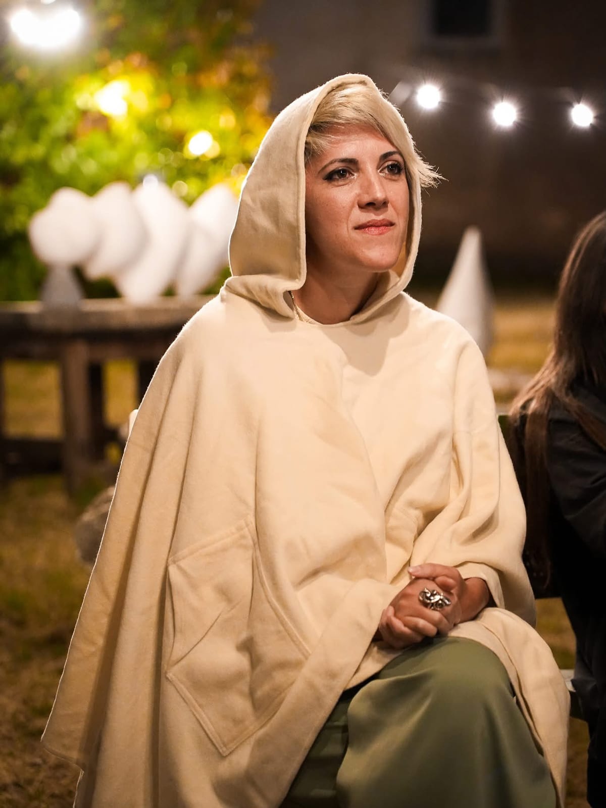Ritratto notturno di Noemi Taccarelli con un saio color panna col cappuccio, sotto luci scintillanti, in una edizione precedente del Ritiro Digitale Spirituale