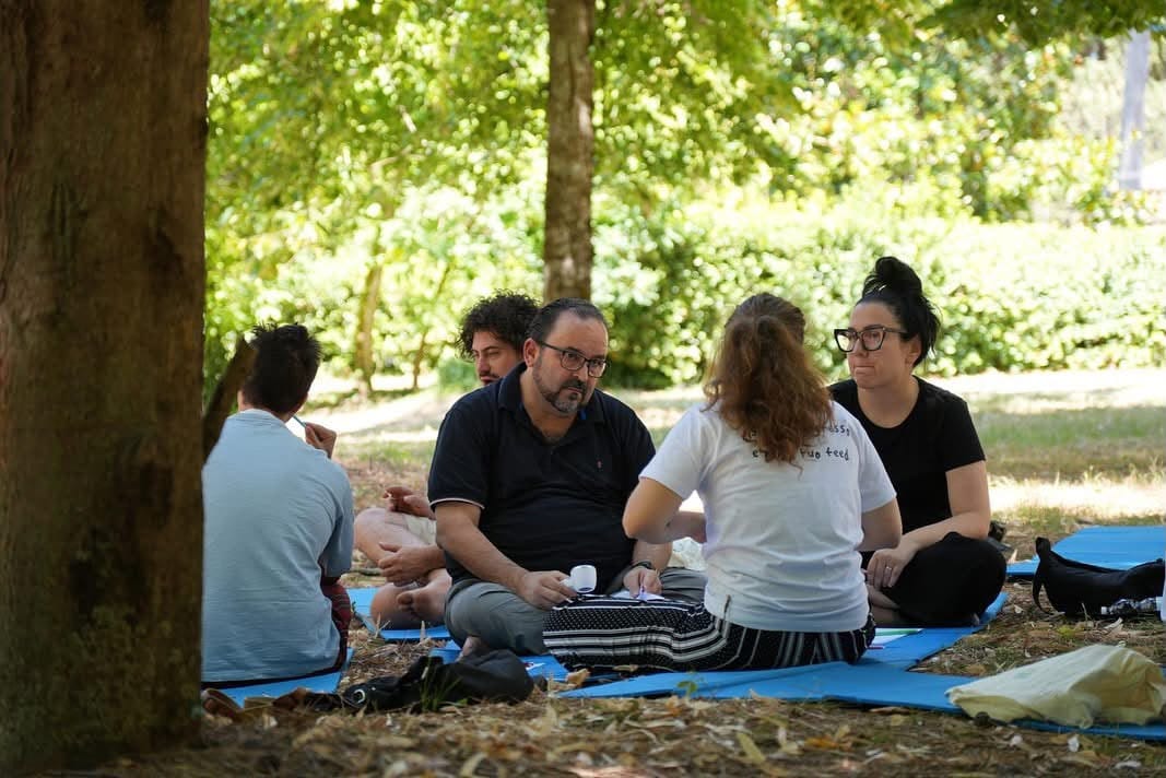 Piccolo gruppo di lavoro in cerchio su un tappetino sotto un albero, durante una sessione di gruppo all'aperto in una edizione precedente del Ritiro Digitale Spirituale a Padula